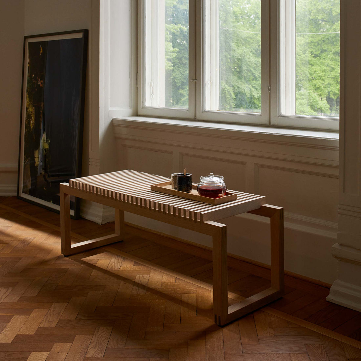 Fritz Hansen Cutter Bench by Niels Hvass. A wooden slat table holds tea items in a sunlit room with large windows.