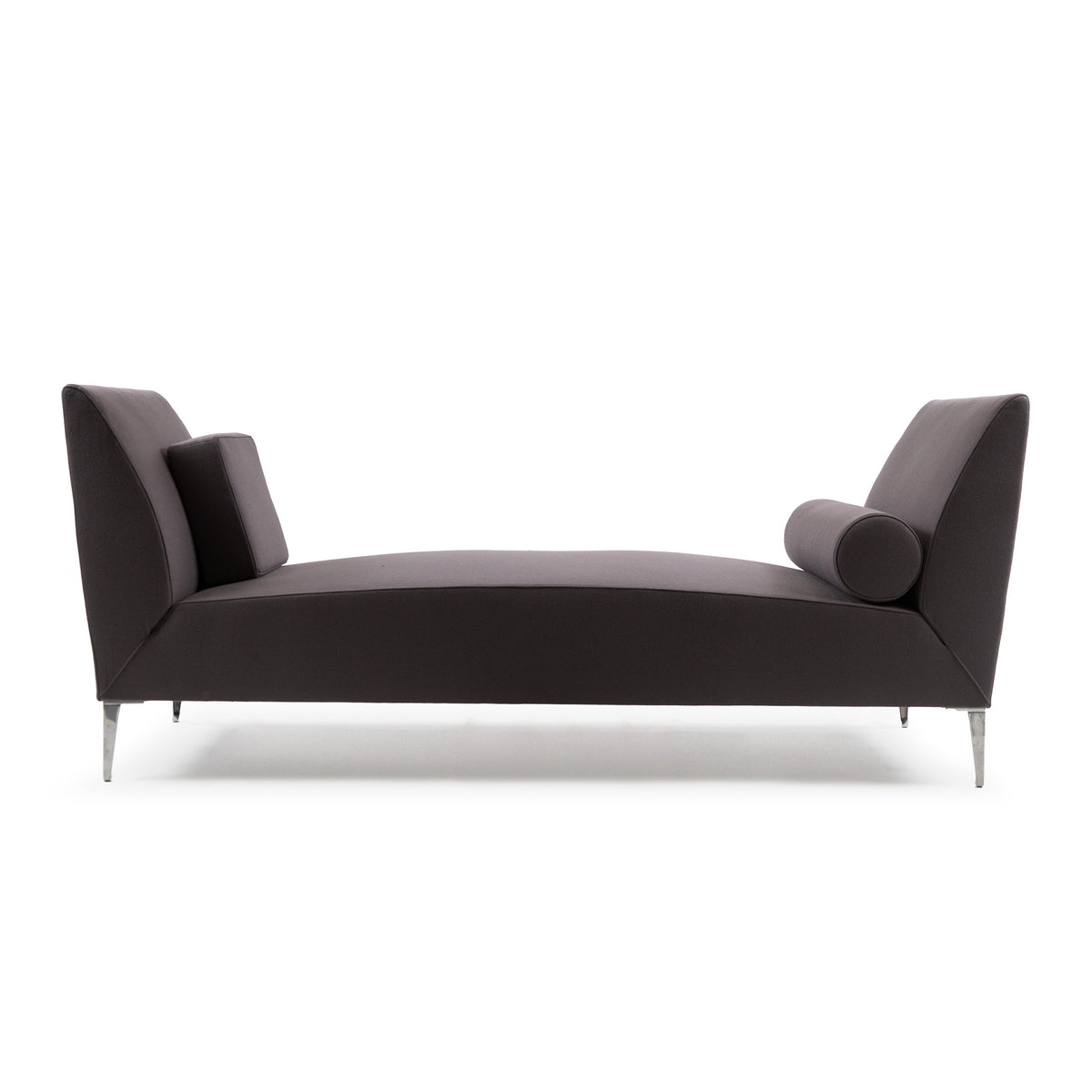 Cappellini Daybed by Jasper Morrison. A curved dark gray upholstered chaise with tapered metal legs and decorative pillows.