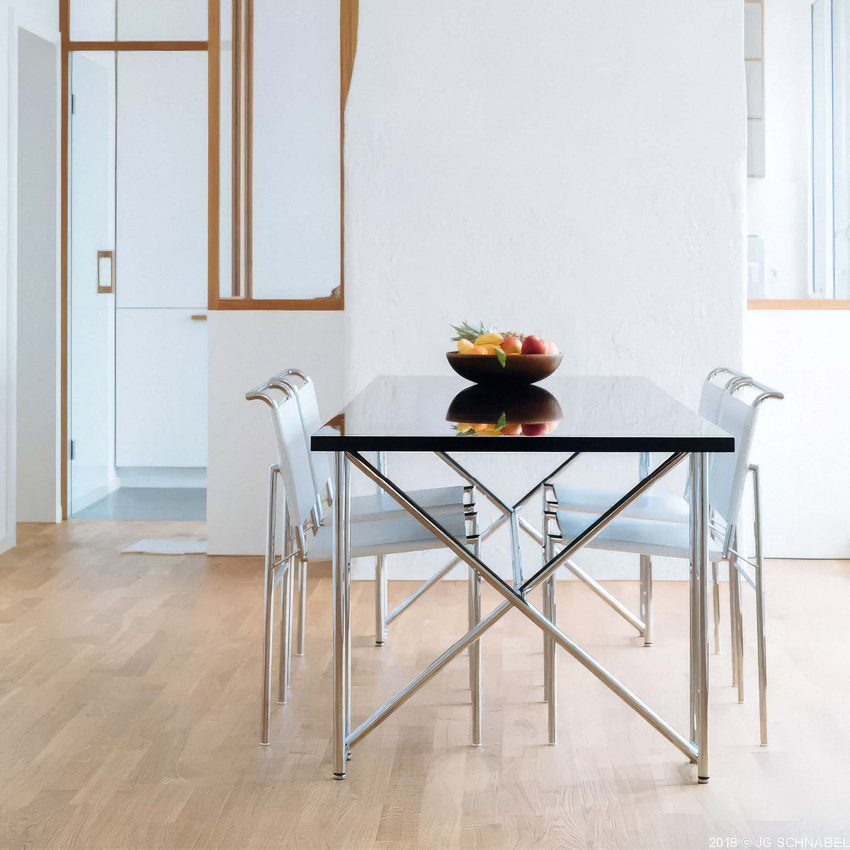 ClassiCon Double X by Eileen Gray. A minimalist dining table with a black top and metal frame holds fresh fruit in a bowl.