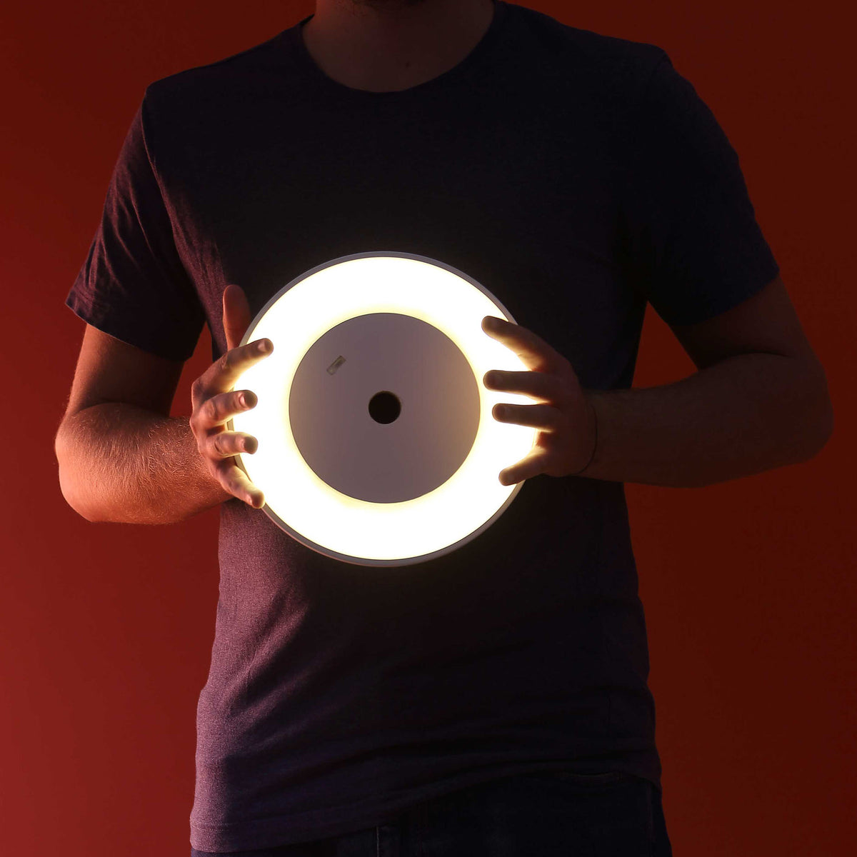COVO Edvige by Enzo Calabrese. A person holds a glowing circular light with a warm white ring against a red background.