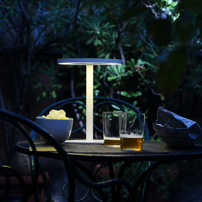 COVO Edvige by Enzo Calabrese. A minimalist white lamp illuminates an evening garden table with drinks and snacks.