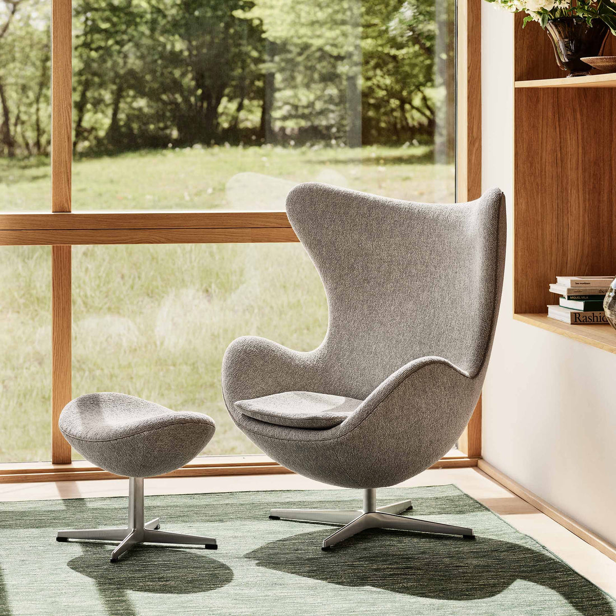 Fritz Hansen Egg™ Chair - 3316 by Arne Jacobsen. A gray fabric chair with ottoman sits by a window overlooking green woods.