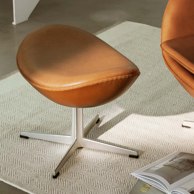 Fritz Hansen Egg™ Foot Stool - 3127 by Arne Jacobsen. Cognac leather chairs with chrome bases sit on a cream carpet.