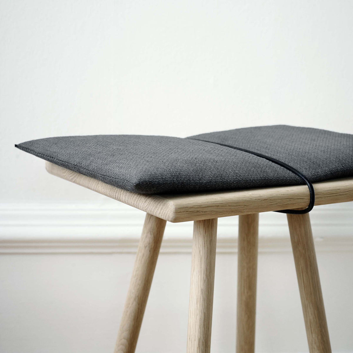 Fritz Hansen Georg Bench by Chris Liljenberg Halstrøm. Light wood stool with gray cushion and black trim.