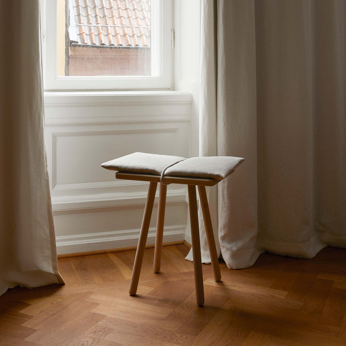 Fritz Hansen Georg Bench by Chris Liljenberg Halstrøm. A wooden stool with beige cushioning sits by a bright window.