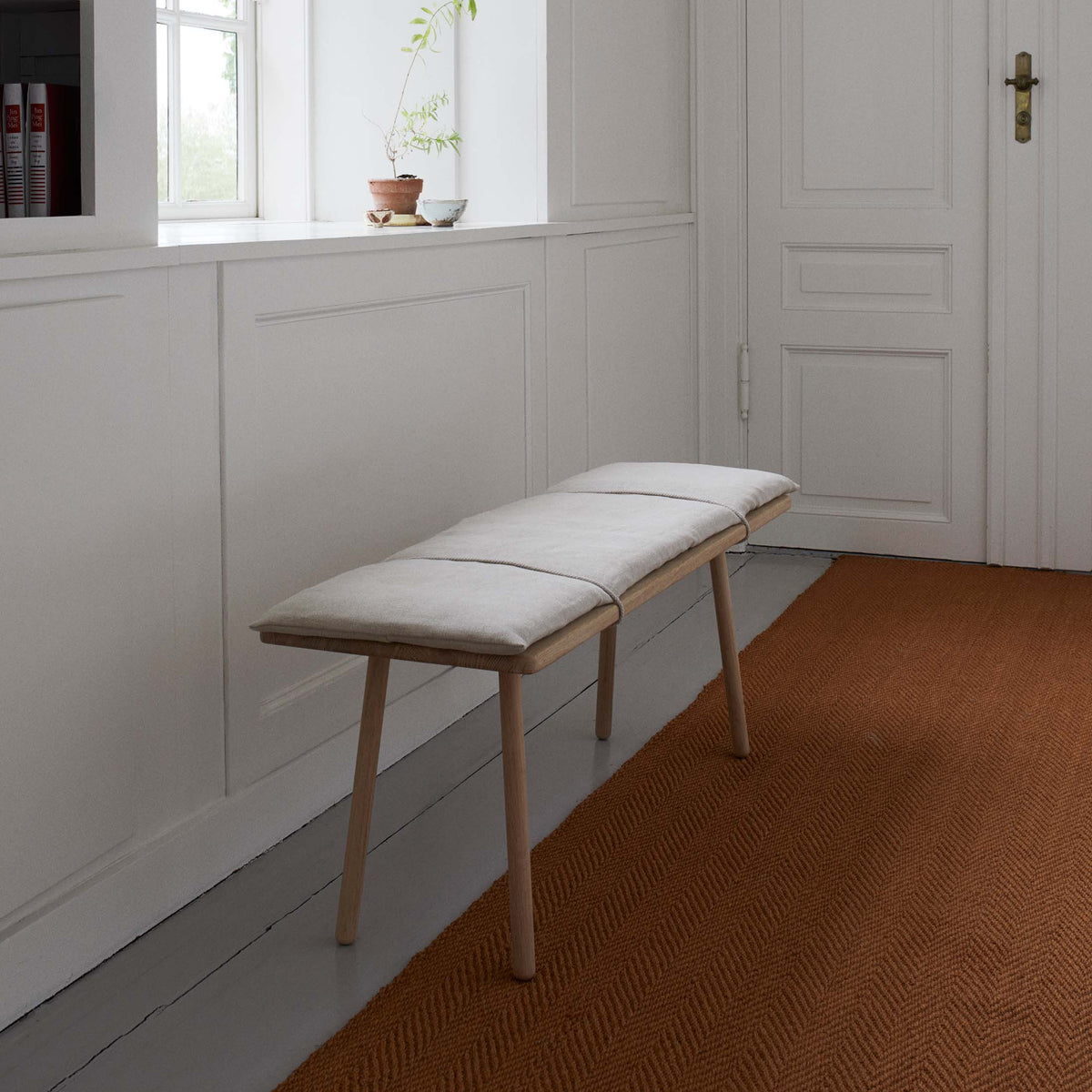 Fritz Hansen Georg Bench by Chris Liljenberg Halstrøm. Wooden bench with cream cushion in minimalist hallway.