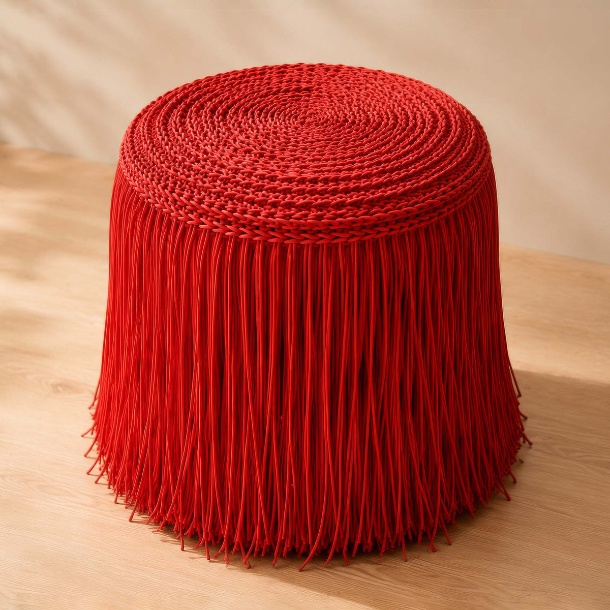 COVO Jelly Pouf by Rosanna Contadini. A vibrant red cylindrical pouf with fringe trim sits on light wooden flooring.