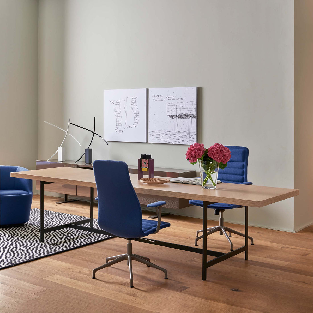 Cappellini Lochness Table by Piero Lissoni. Modern office space features wooden desk, blue chairs, and pink flowers.