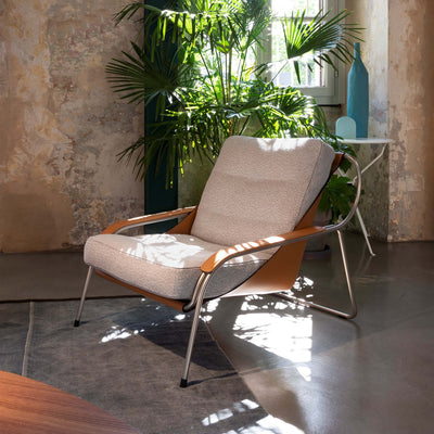 Zanotta Maggiolina by Marco Zanuso. A modern chair with beige cushions and wooden armrests sits in sunlit room with plants.