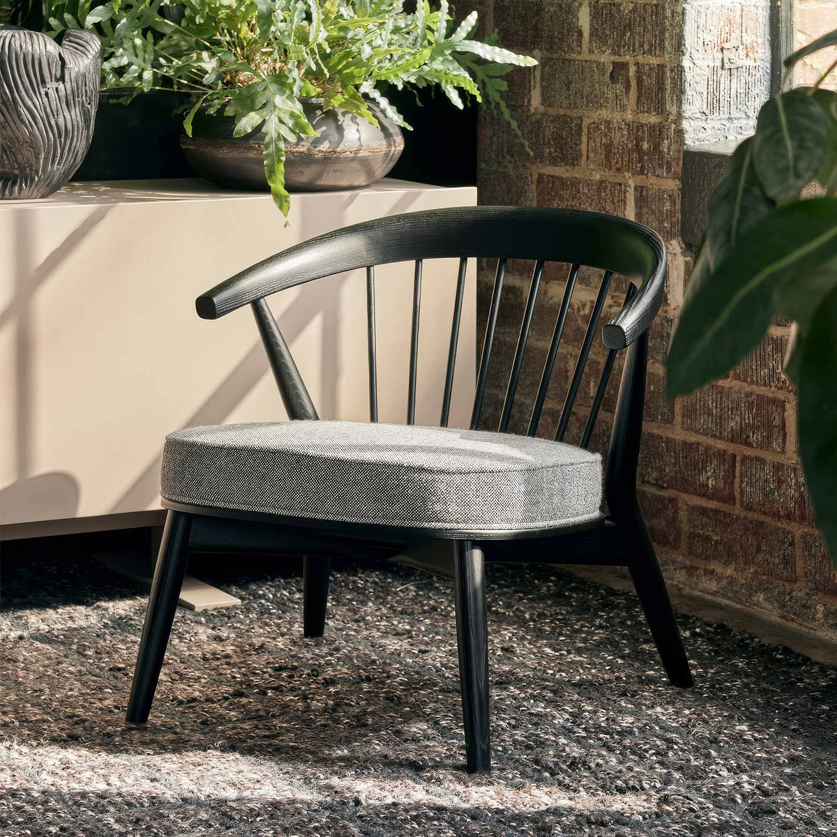 Cappellini Newood Relax by BrogliatoTraverso. A black wooden chair with a grey cushioned seat sits in a sunny garden patio.