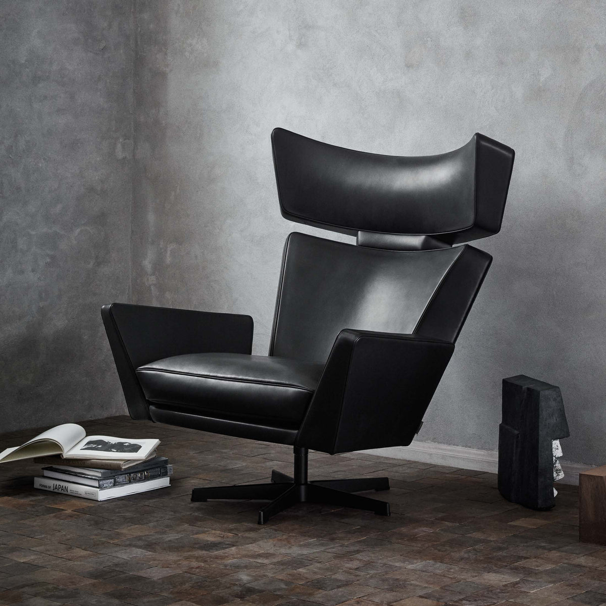 Fritz Hansen Oksen™ Armchair 4201 by Arne Jacobsen. A sleek black leather chair sits in a minimalist gray concrete interior.