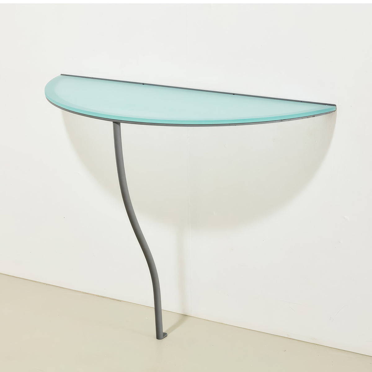 Cappellini One Legged Table by Jasper Morrison. A curved glass-topped console table with a sleek gray metal leg.