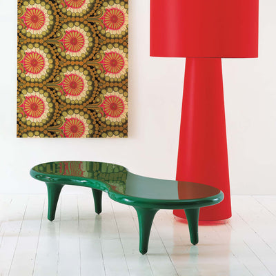 Cappellini Orgone Table by Marc Newson. A green curved bench sits beside a red lamp in a bright gallery space.