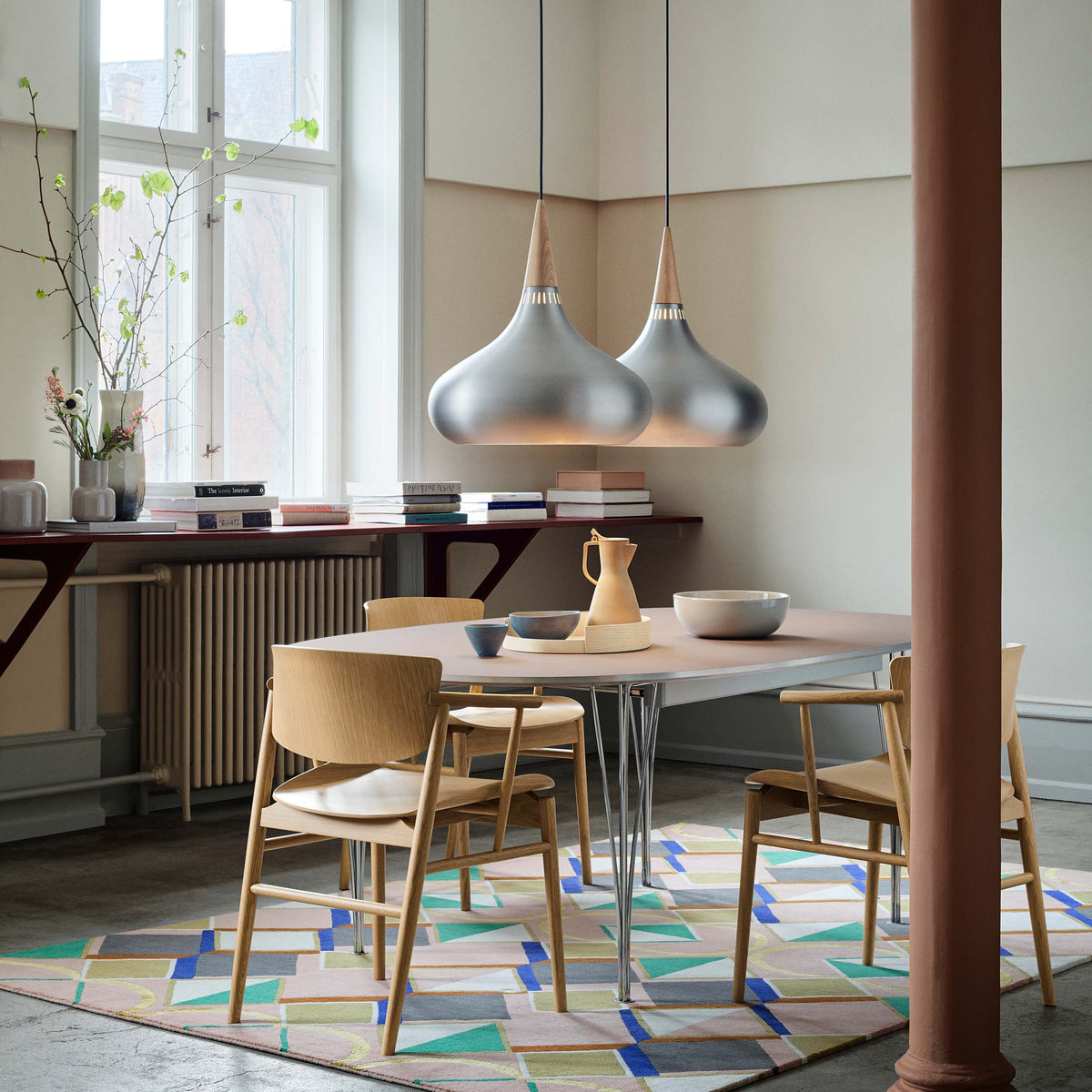 Fritz Hansen Orient™ Pendant - P2, Ø 340 mm by Jo Hammerborg. Two silver pendant lights hang above a wooden dining table.