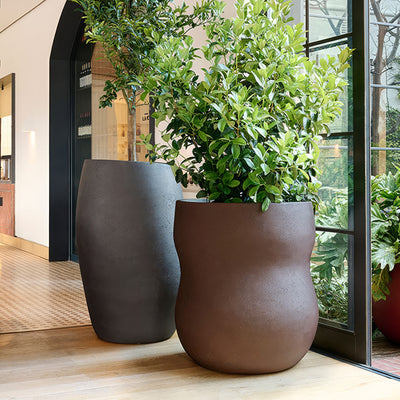 Indigenus Pebble by Glenn Pushelberg & George Yabu. Two textured brown planters with green plants in a modern interior space.