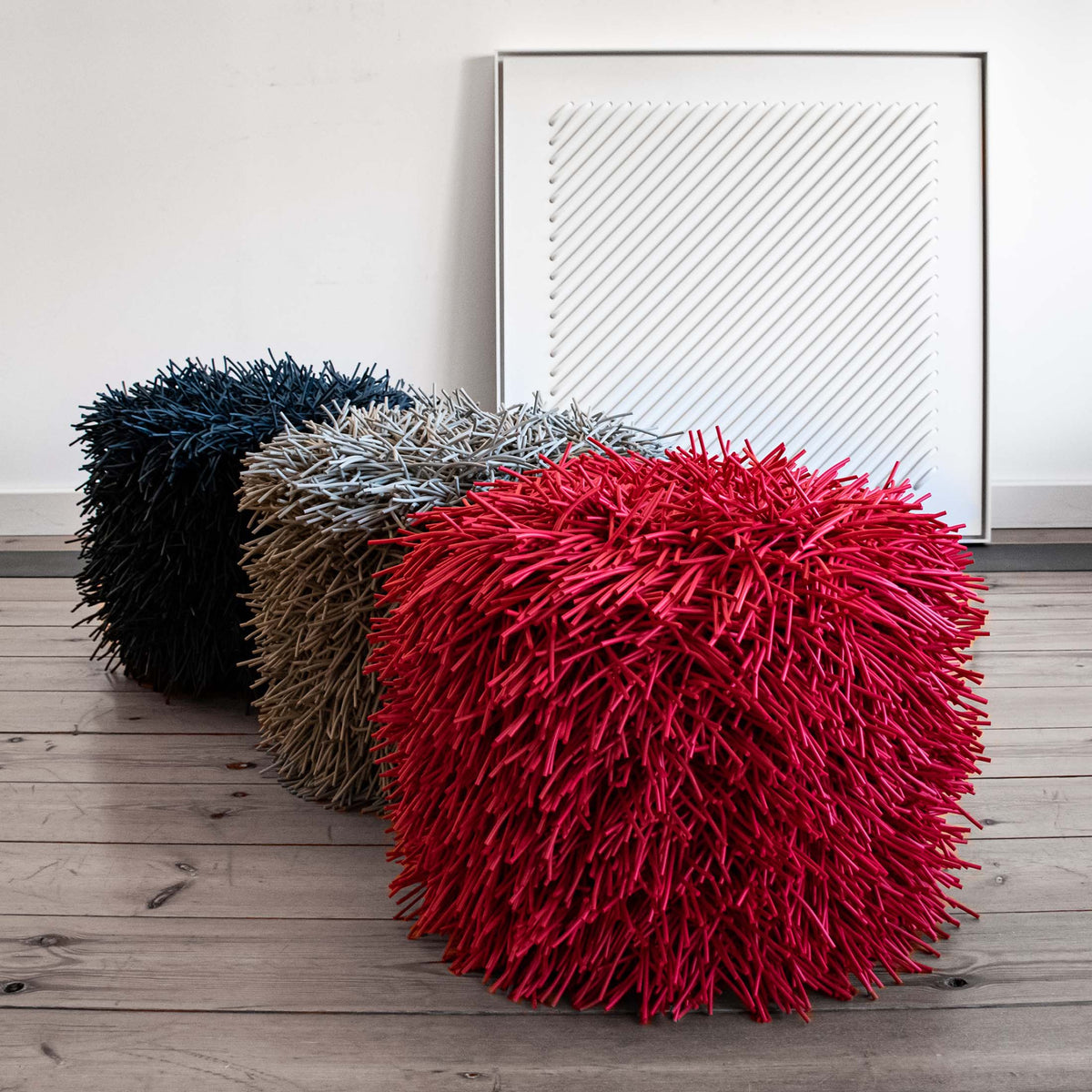 COVO Porcupine Pouf by Rosanna Contadini. Three spiky poufs in black, tan, and red sit on wooden flooring.