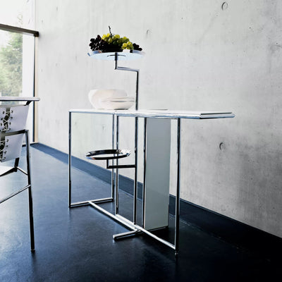 ClassiCon Rivoli by Eileen Gray. A sleek metal stand with glass shelves holds grapes and dishware in a minimalist interior.