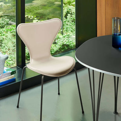 Fritz Hansen Series 7™ Chair 3107 by Arne Jacobsen. A cream chair with metal legs sits beside a black round table by windows.