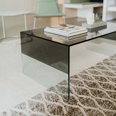 Cappellini Smoke by Marcel Wanders. A sleek black glass table sits in a modern living room with neutral tones.