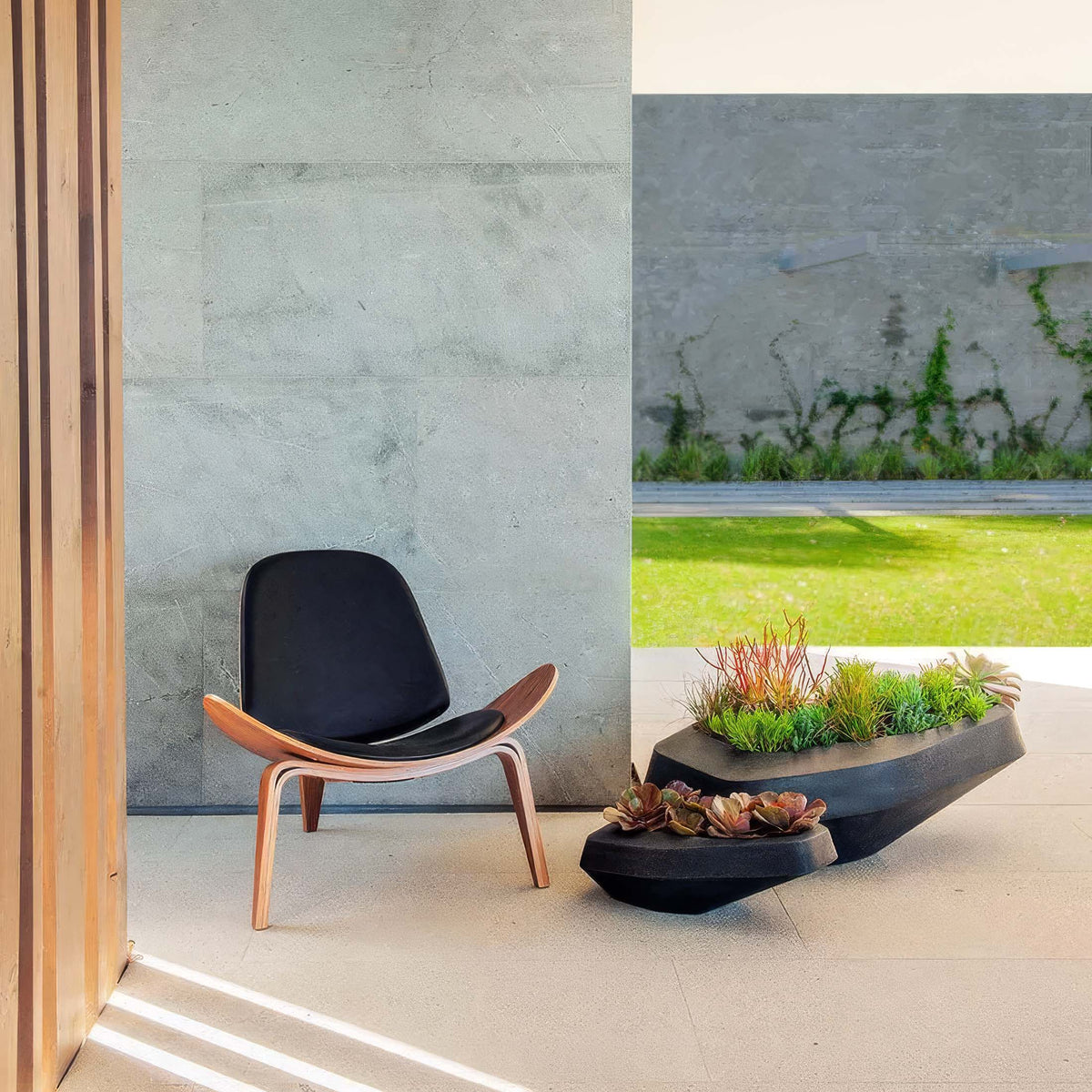 Indigenus Steen by Stefan Antoni and Greg Truen. A wooden-framed lounge chair with black cushioning sits on a concrete patio.