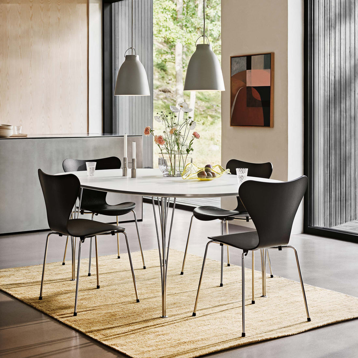 Fritz Hansen Superellipse™ B611 Table by Piet Hein. A modern dining space features black chairs around a white oval table.
