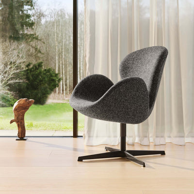 Fritz Hansen Swan™ Chair by Arne Jacobsen. A gray upholstered chair sits in a bright room overlooking forest views.