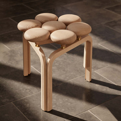 Fritz Hansen JU01™ Utzon Stool by Jørn Utzon. Light wood stool with seven rounded seats on a tile floor.