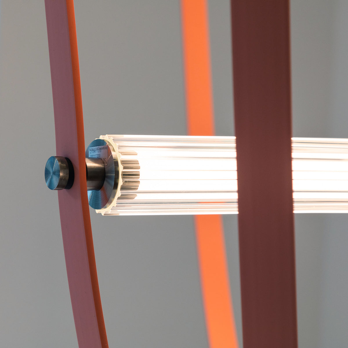 Flos Wireline by Formafantasma. A metallic connector with a blue dial attaches a ribbed white rod to angled colored panels.