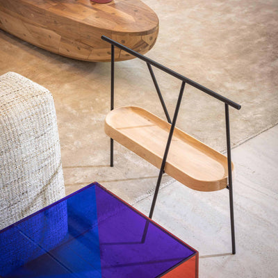 Cappellini Pinch by Nendo. A wooden chair with black metal legs sits on concrete flooring beside upholstered furniture.