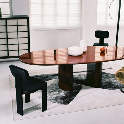Cappellini Selettiva Cantù by Giulio Cappellini. A polished wooden oval table with dark pedestals sits in a minimalist room.