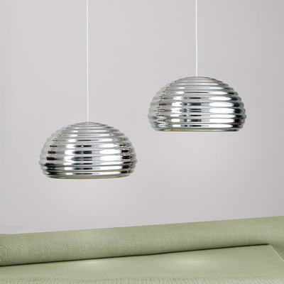 Flos Splügen Bräu by Achille Castiglioni. Two reflective glass pendant lights hang above a pale green upholstered surface.