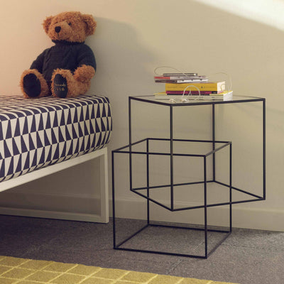 Cappellini Thin Black Table by Nendo. A black metal frame table holds stacked books beside a teddy bear on a striped bed.